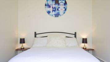 A neatly made bed with white linens, two bedside lamps, and a circular abstract painting above the headboard.