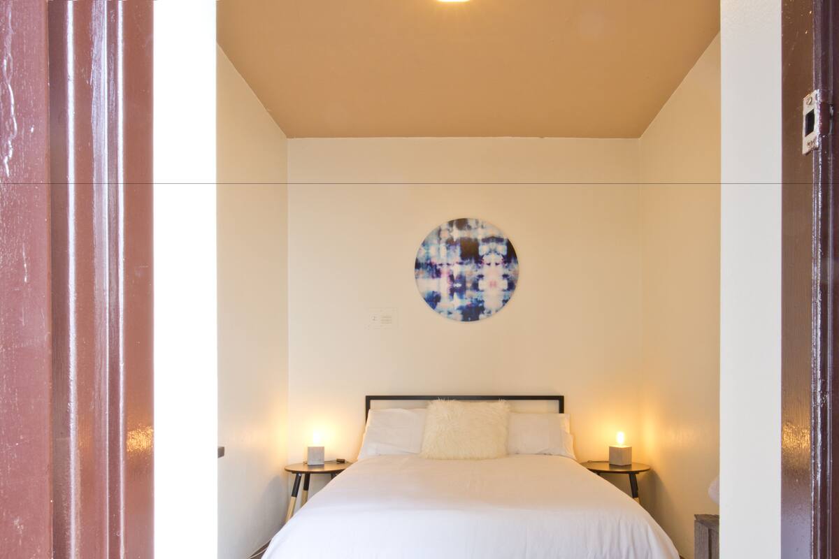 Een slaapkamer met een bed, twee nachtkastjes, een wandklok en een rond kunstwerk erboven.
