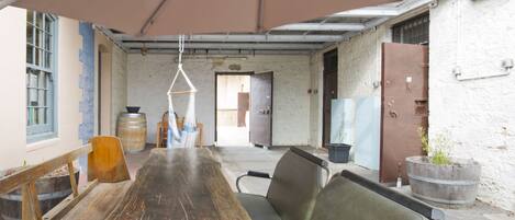 A long wooden table with metal chairs, a hanging light fixture, and a large window with blue shutters.