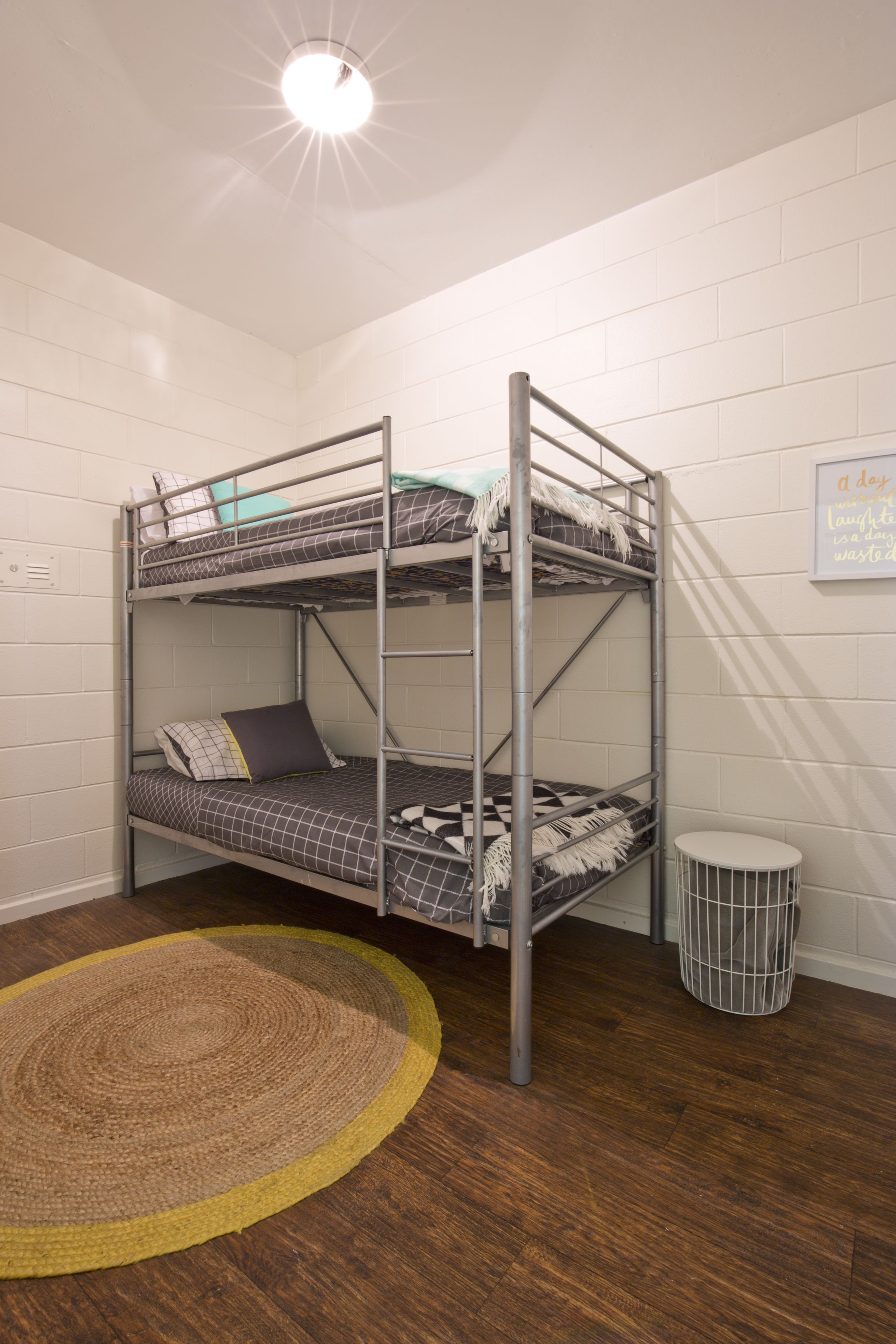 A bunk bed room with a round rug, a waste bin, and a motivational quote on the wall.