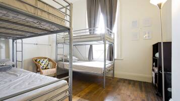 A dormitory room with bunk beds, a chair, a desk, and a lamp.