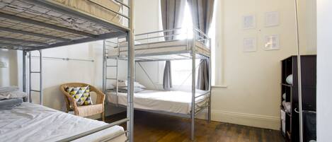 A dormitory room with bunk beds, a chair, a desk, and a lamp.