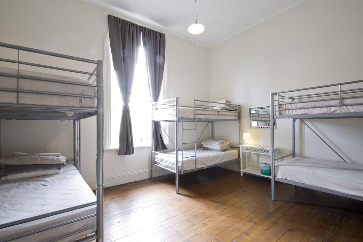 Een slaapzaal met stapelbedden, een raam met gordijnen, een hanglamp en een houten vloer.