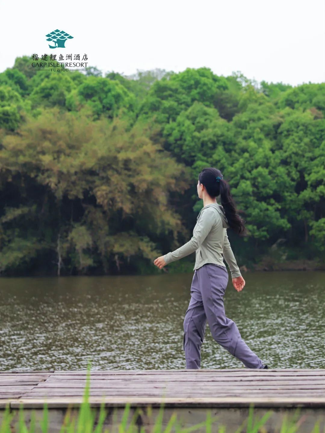 A person walking on a wooden dock by a lake with dense greenery in the background.