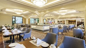 Un vaste espace de restauration dans l’hôtel, avec de nombreuses tables et chaises, un bar central et une grande fenêtre offrant une vue sur l’extérieur.