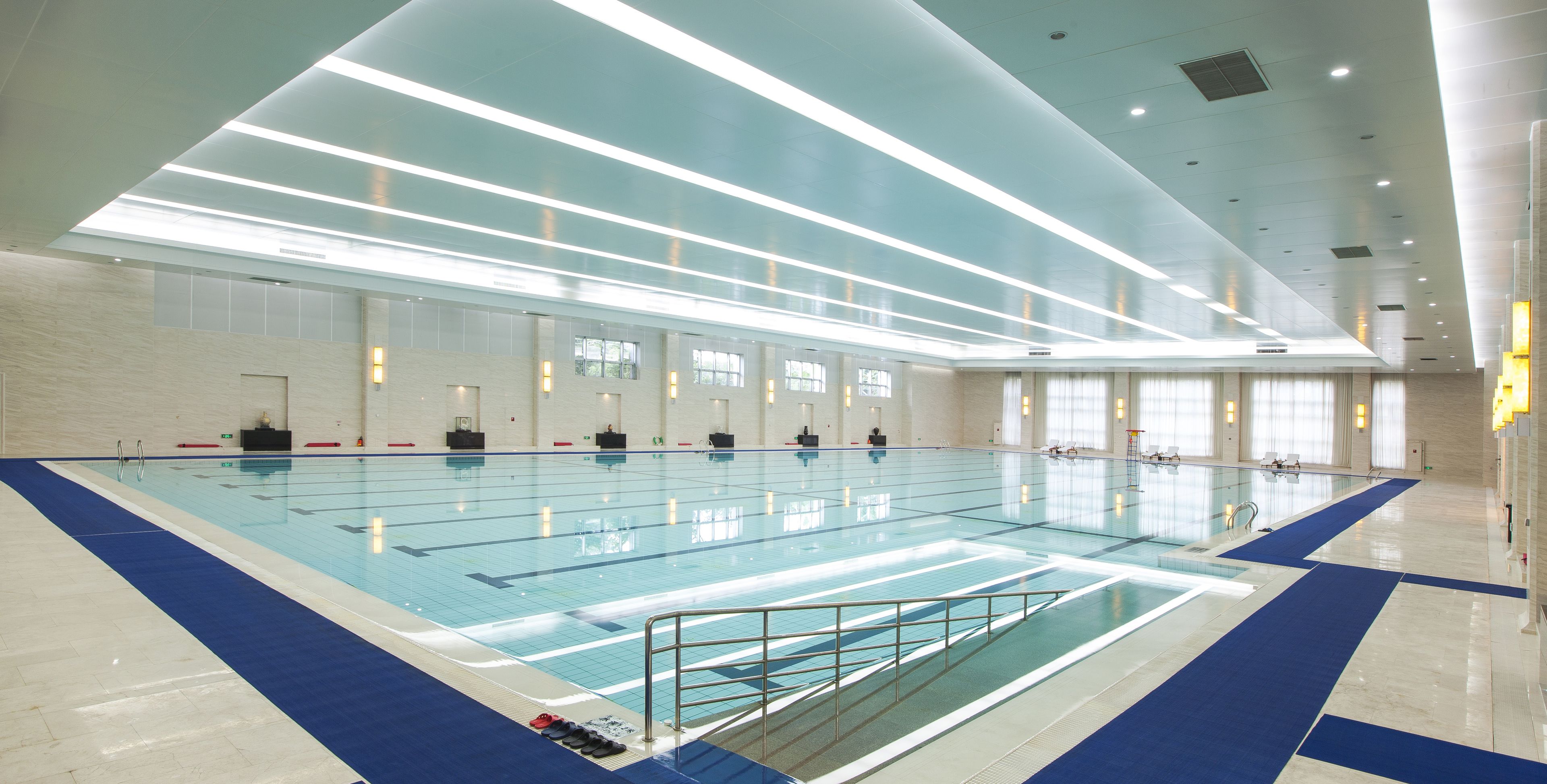 An indoor swimming pool with clear lanes, a blue and white tiled floor, and overhead lighting.