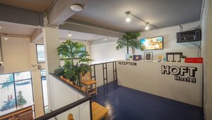A reception area with a reception desk labeled "HOFT Hostel," a plant, a TV mounted on the wall, and a staircase leading to another floor. - Arawana Hostel Silom (Bangkok)