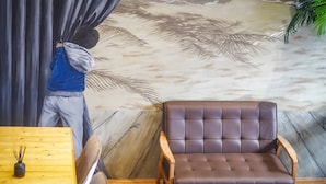 A room with a mural of palm leaves on the wall, a brown leather chair, and a wooden table with a bottle. - Arawana Hostel Silom (Bangkok)