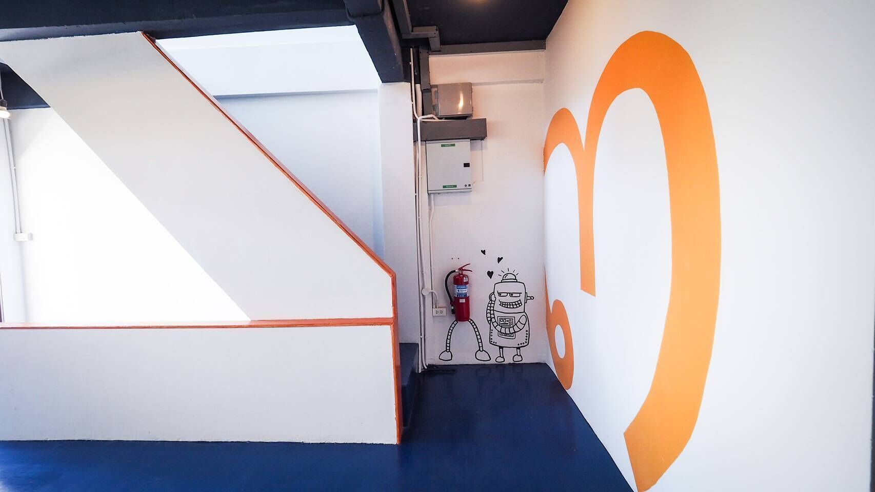 A modern interior with a white and orange color scheme, a staircase, and a fire extinguisher on the wall.