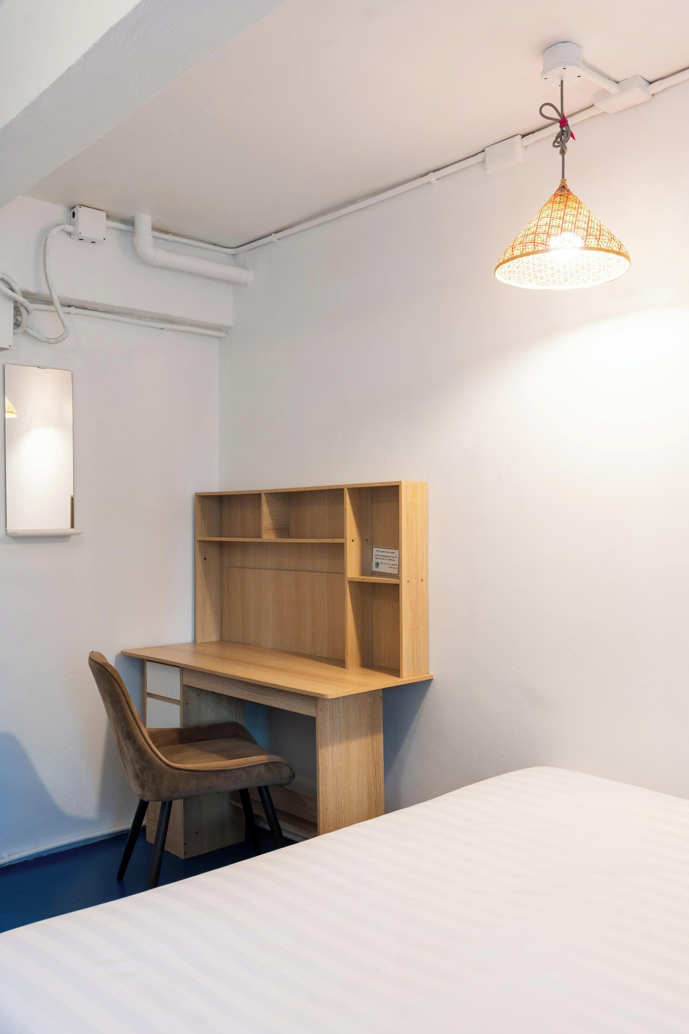 A room with a wooden desk, a chair, a bed, and a hanging light fixture.