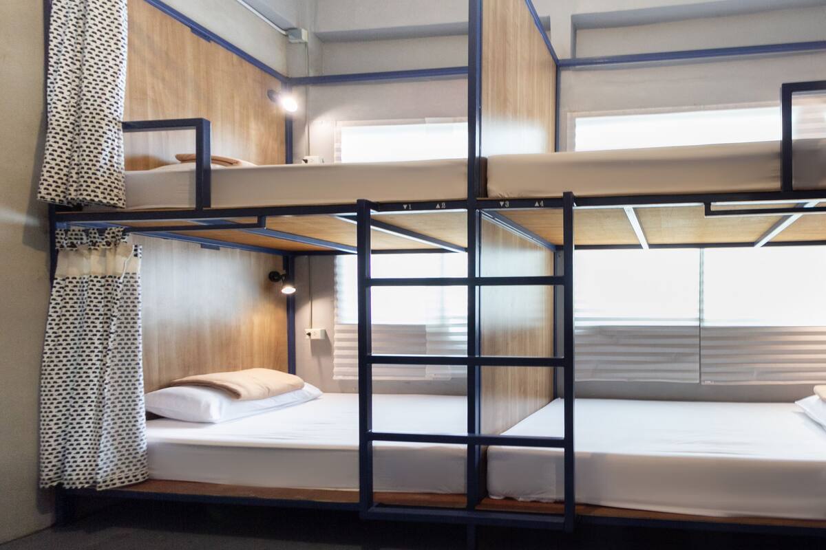 Habitación con literas, una escalera, cabecero de madera y una ventana con persianas.