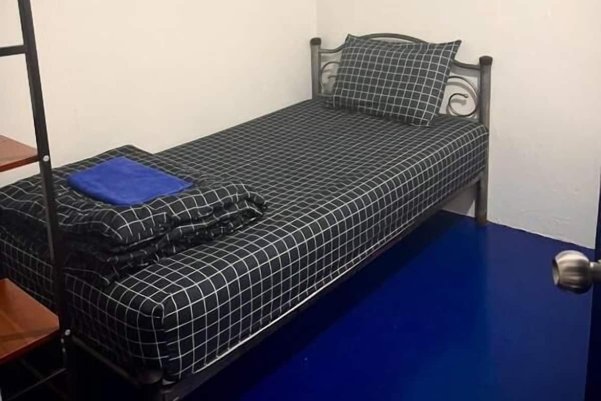 Una habitación pequeña con una cama individual, estructura metálica y un cubrecolchón estampado de cuadros.