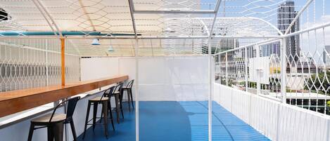 An indoor seating area with a blue floor, white metal railings, and a wooden bench.