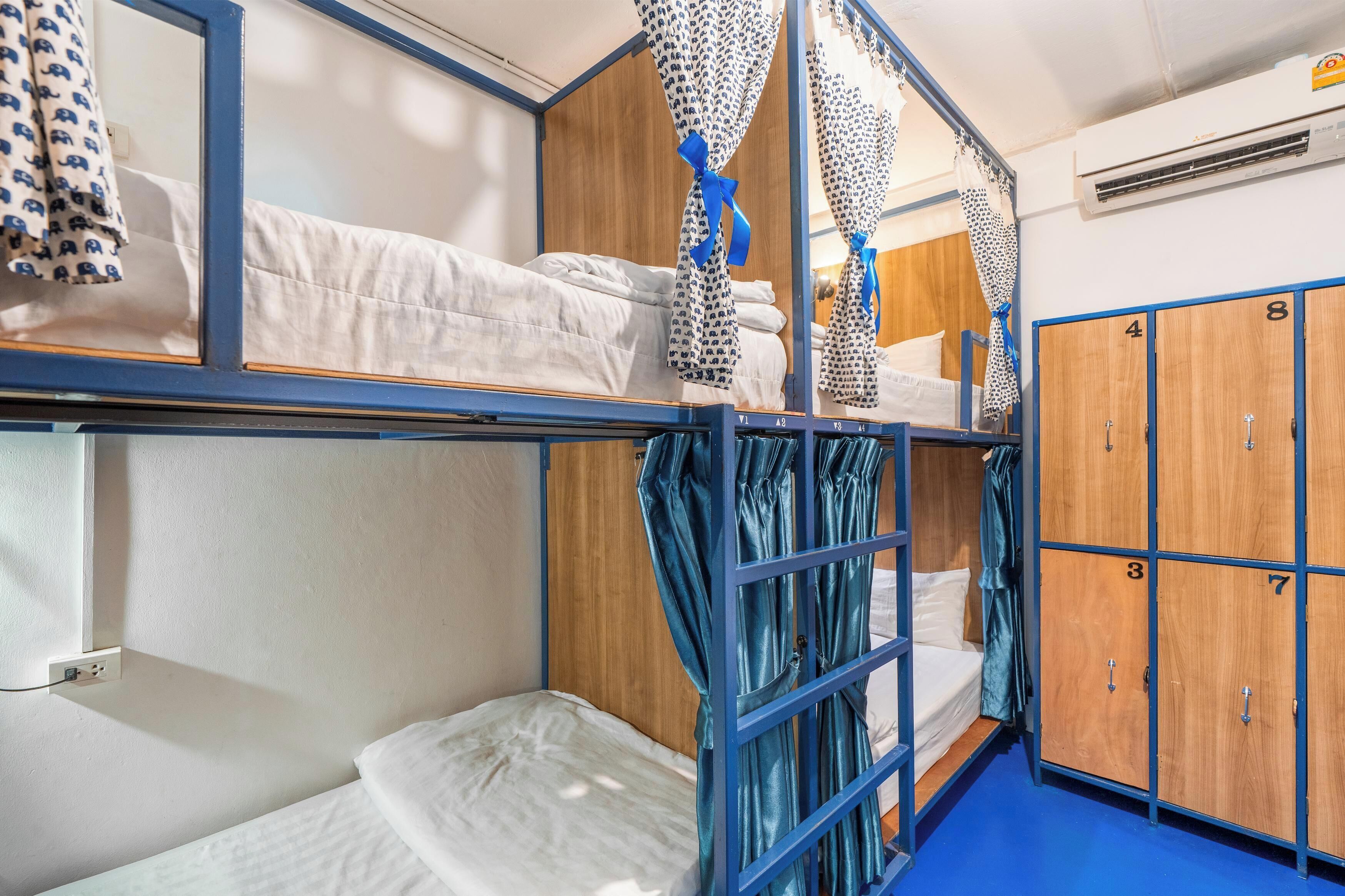 Ein Schlafraum mit Etagenbett, blauer Rahmen, Holzschrank und gemusterten Vorhängen.