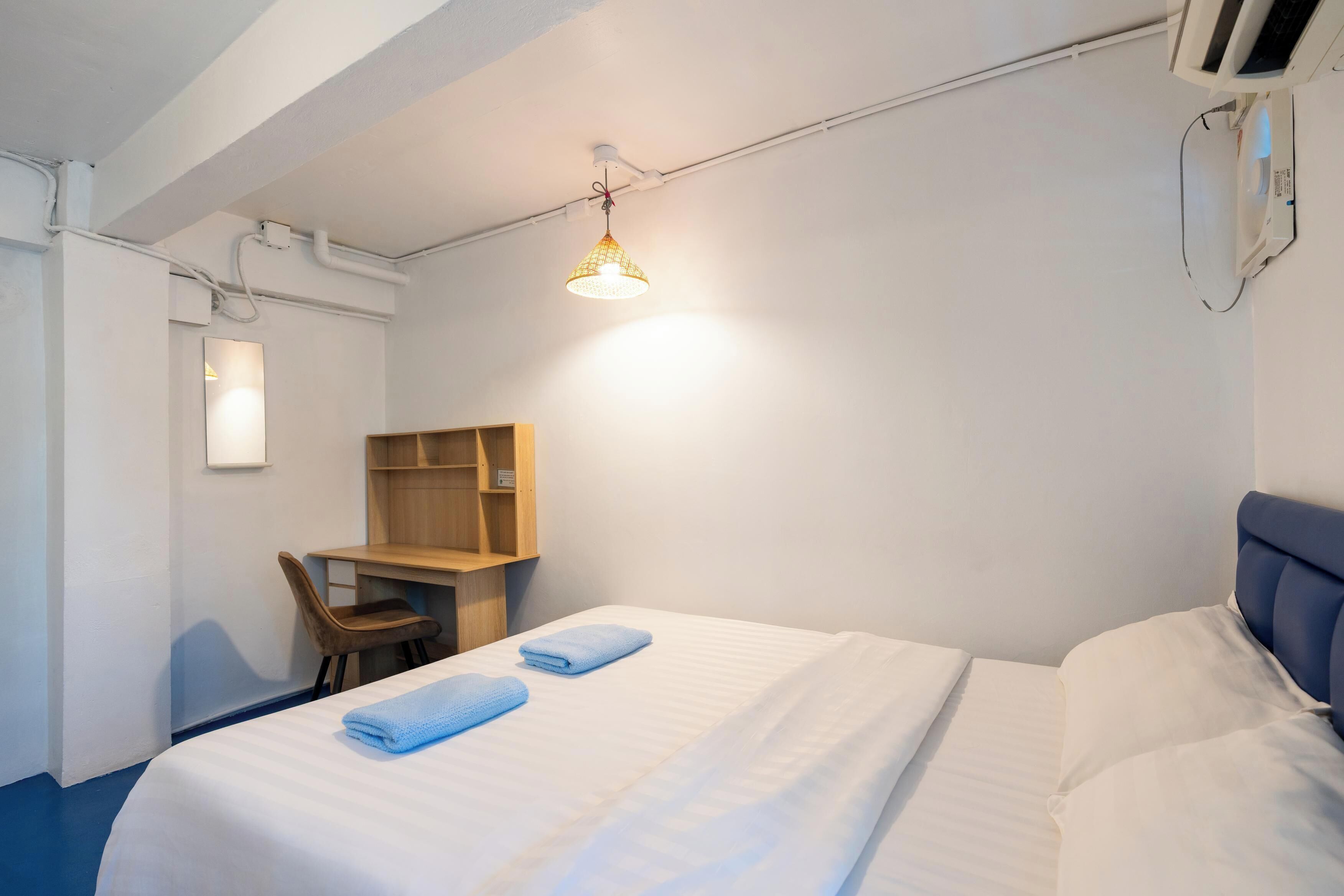 A hotel room with a bed, a desk, a chair, and a hanging light fixture.