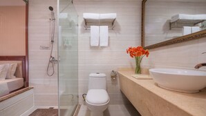 Une salle de bain moderne avec une douche à parois de verre, des toilettes blanches, un plan de toilette beige doté d’un grand lavabo et un miroir au-dessus du lavabo.
