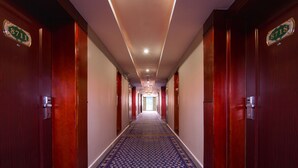 Un couloir d’hôtel avec un tapis à motifs, des portes en bois et un numéro de chambre sur chaque porte.