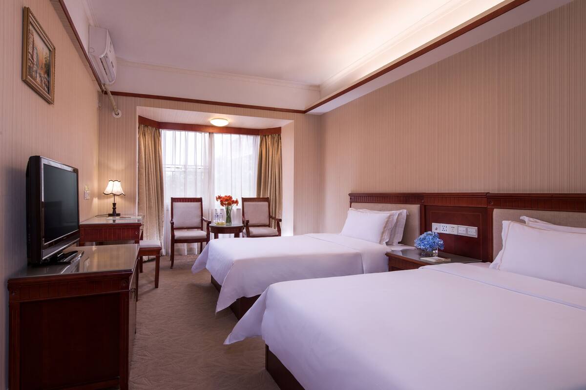 Une chambre d’hôtel avec deux lits, une télévision, un bureau avec une lampe et une fenêtre avec des rideaux.