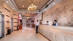Un hall d’hôtel avec un comptoir de réception en marbre, un lustre et une fresque représentant des anges sur le mur.