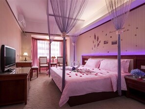 Une chambre d’hôtel avec un lit à baldaquin, une télévision, un bureau et une chaise.