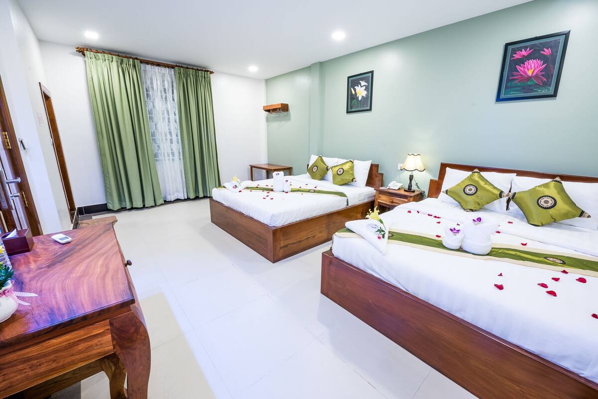 Une chambre d’hôtel avec deux lits, un bureau en bois et un rideau vert.