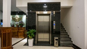 Un ascensor en un vestíbulo con un muro de mármol, un basurero y una escalera.