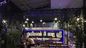 Un espacio interior con mesas y sillas, un letrero de neón y plantas colgantes.