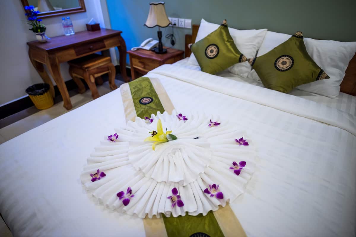 Un lit bien fait, agrémenté d’un arrangement floral et d’un coussin décoratif vert.