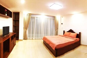 Un dormitorio con una cama, un televisor sobre un soporte de madera y una ventana con cortinas.