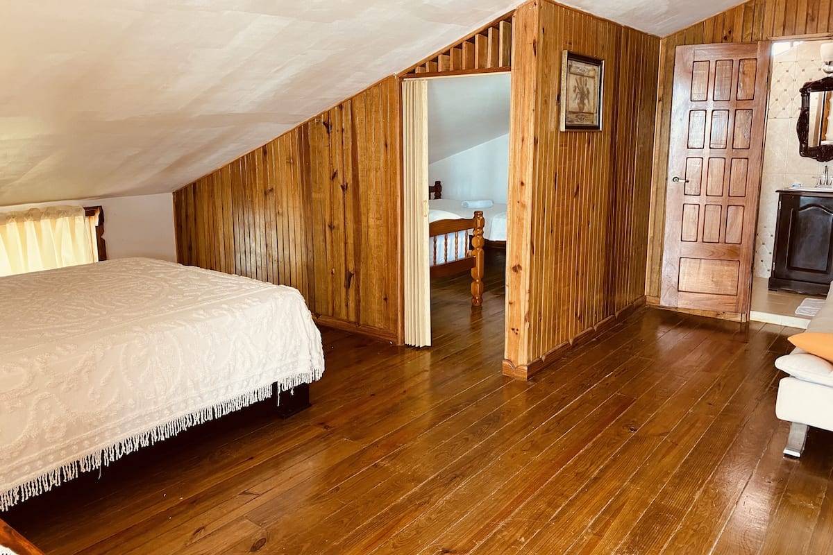 Un dormitorio con techo inclinado de madera, una cama con cubrecama blanco y una puerta de madera con un cuadro.