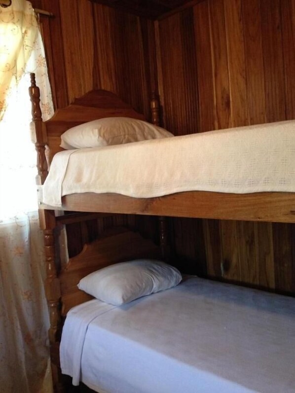 A wooden bunk bed with white bedding in a room with wooden walls.