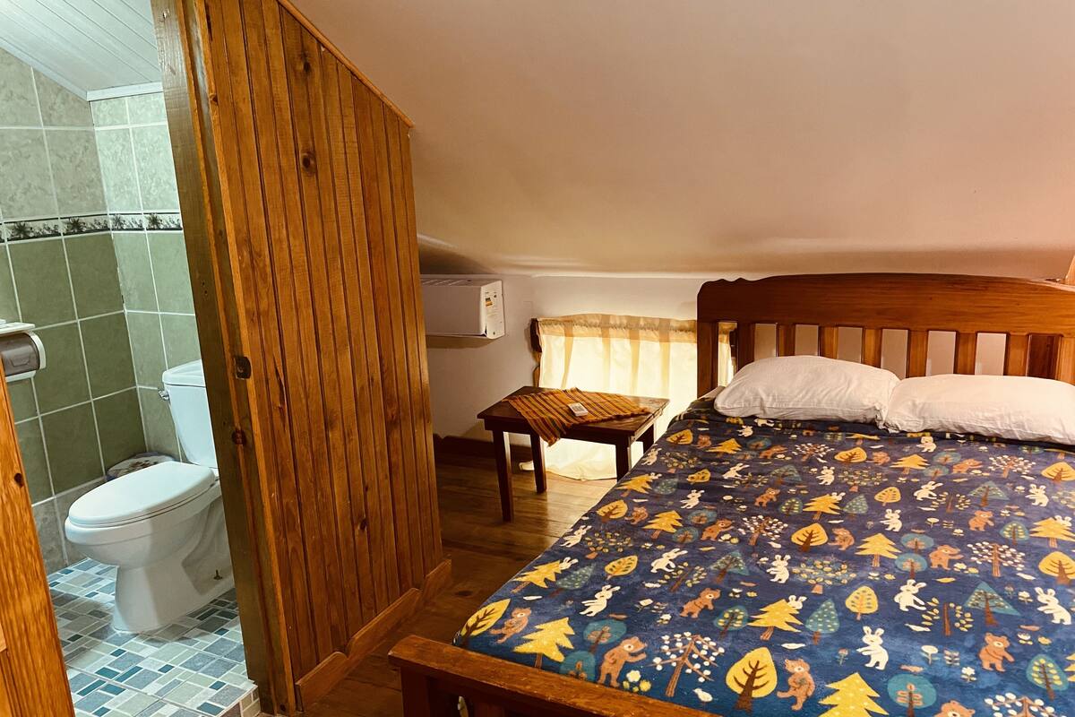 Un dormitorio con una cama de madera, una mesita de noche pequeña y una ventana con cortinas.