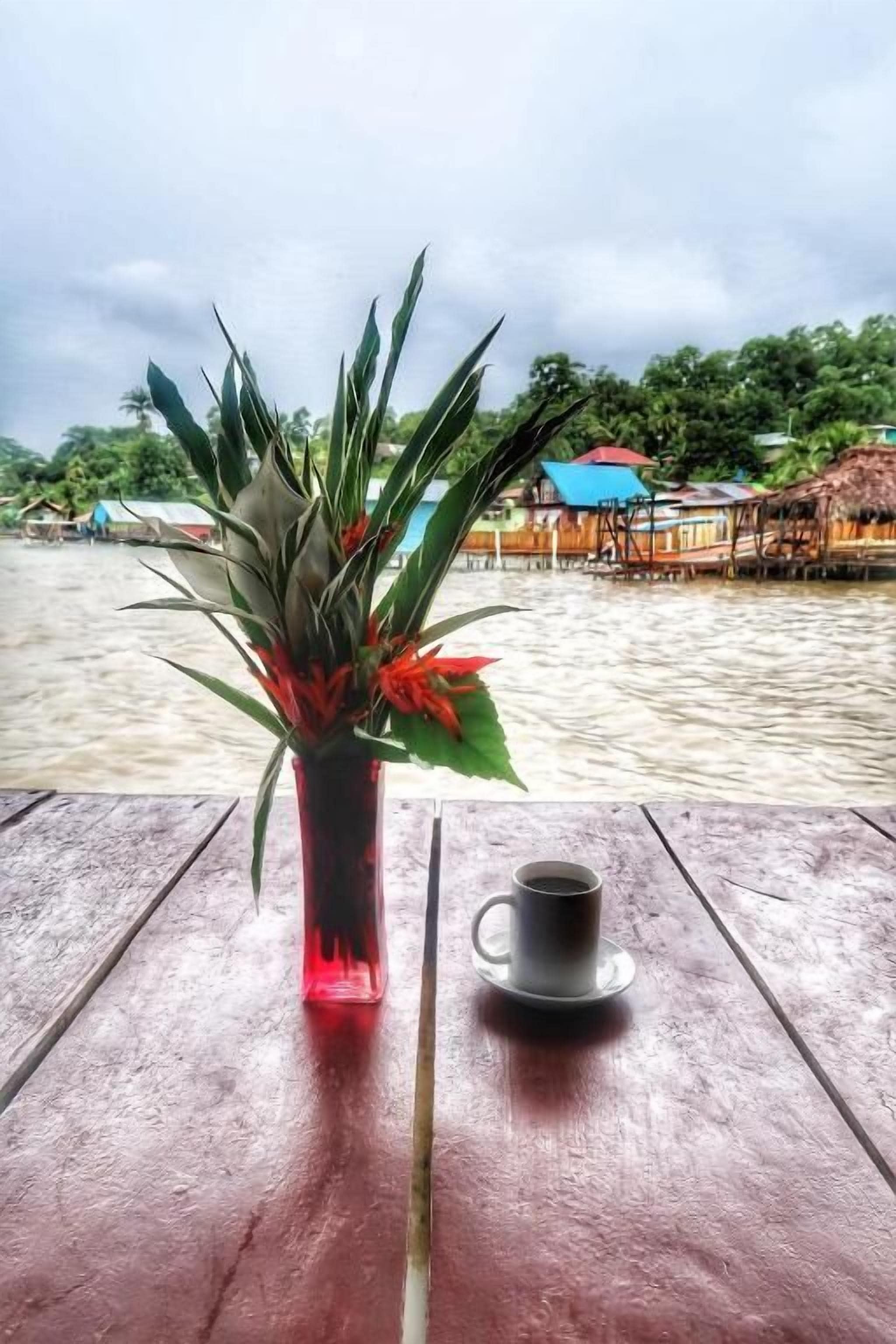 A wooden table with a red vase containing a plant and a cup.