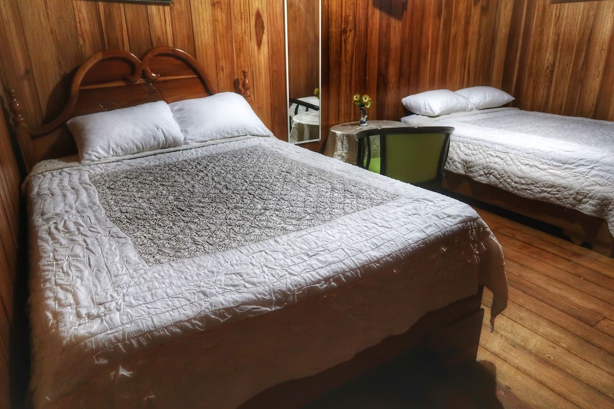 Una habitación con paneles de madera y dos camas, cada una con cubrecama y almohadas blancas acolchadas.