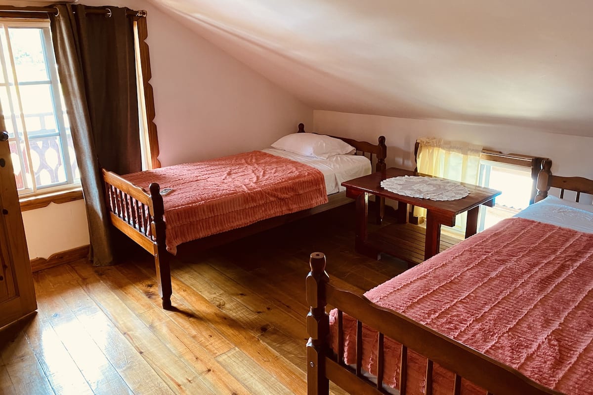 Una habitación con dos camas de madera, una mesa de madera y un ventanal con cortinas.