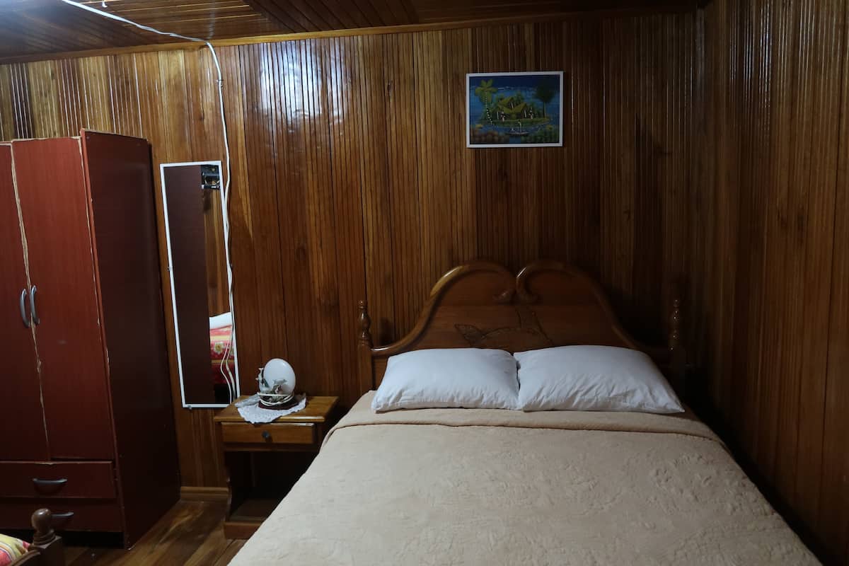 Una habitación con paneles de madera, una cama, una mesita de noche, un armario y un cuadro en la pared.