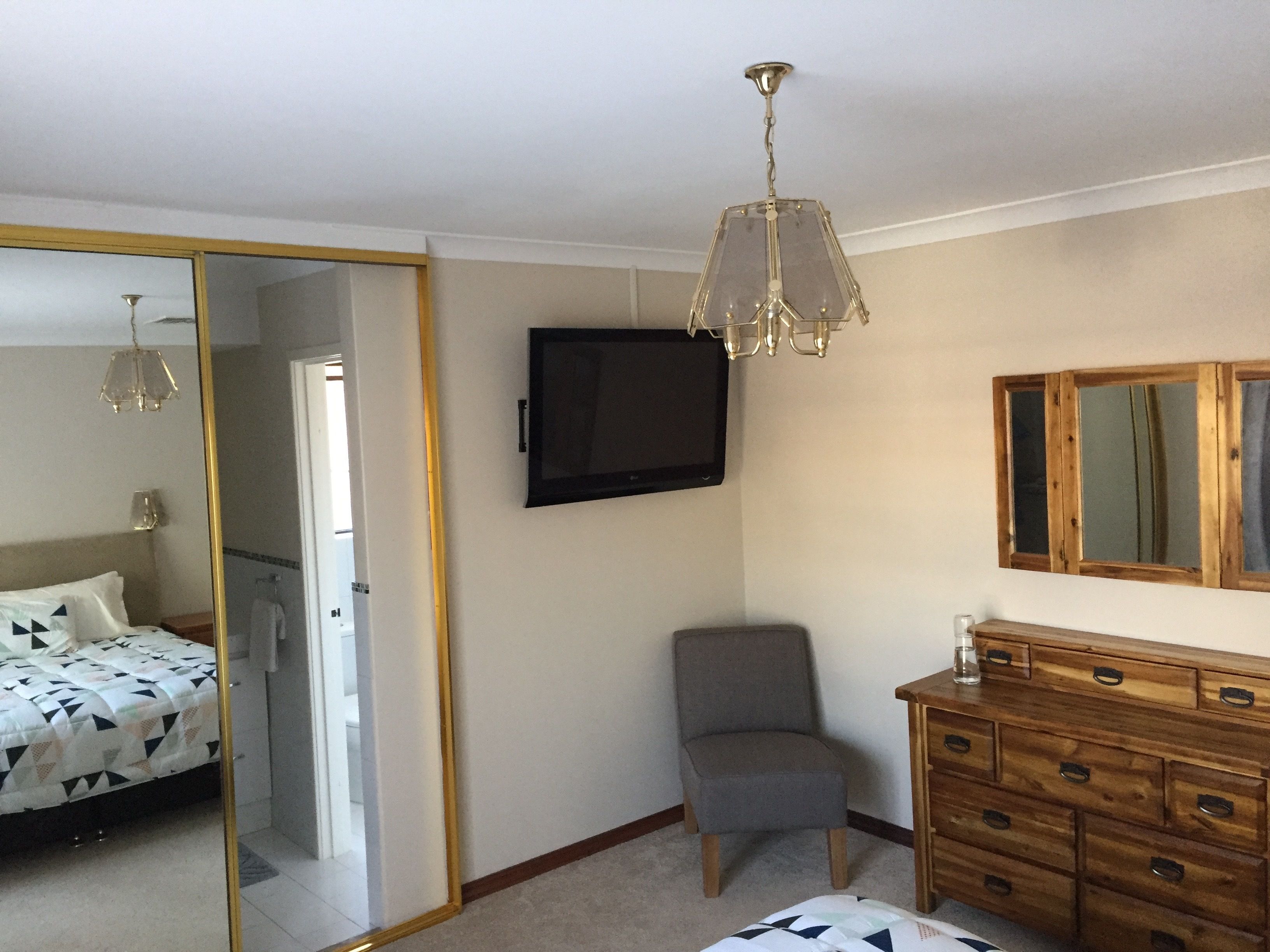 A bedroom with a bed, a chair, a dresser, a TV, and a mirror.