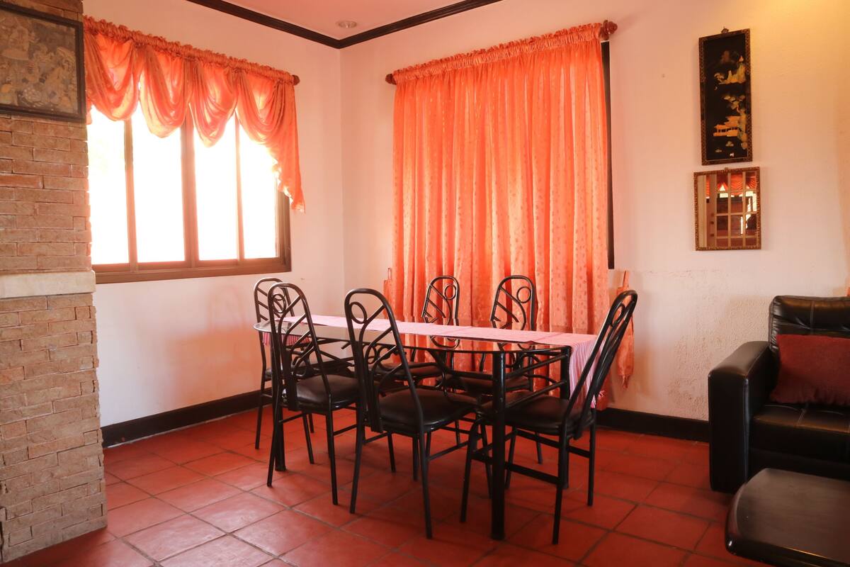 Un coin repas avec un mur en briques, un sol carrelé, une table avec des chaises et des rideaux orange.