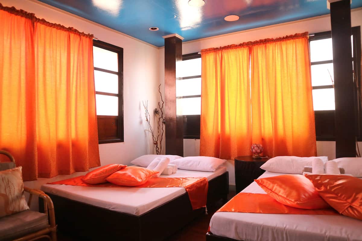 Une chambre d’hôtel avec deux lits, des rideaux orange, du linge de lit blanc et une tête de lit en bois.