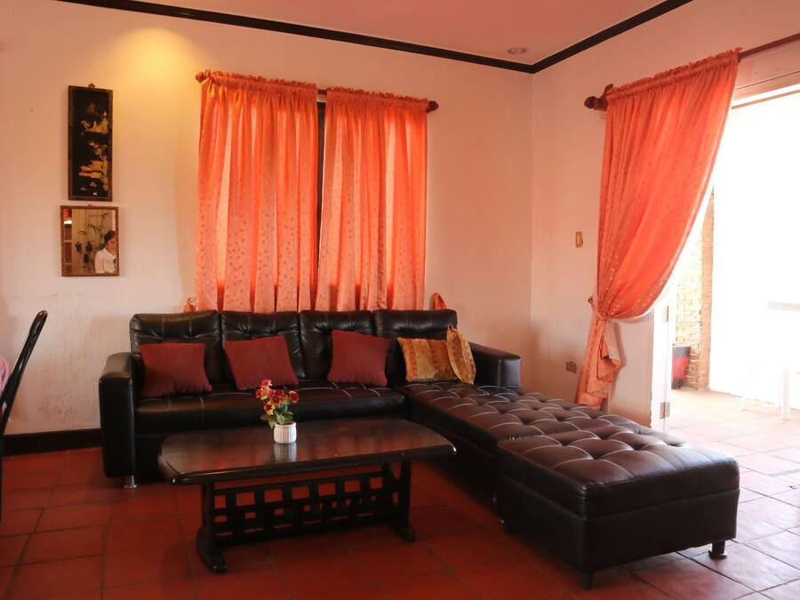 Una sala de estar con un sofá de cuero negro, una mesa de centro y cortinas anaranjadas.