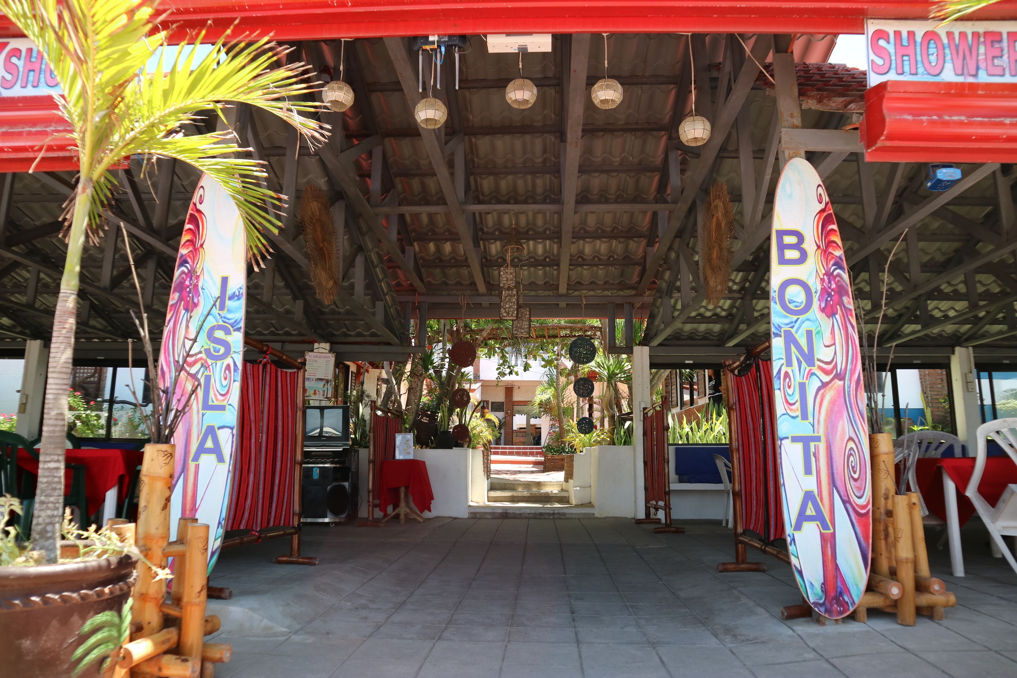 Un espacio techado con tablas de surf, un letrero de ducha y un toldo rojo.