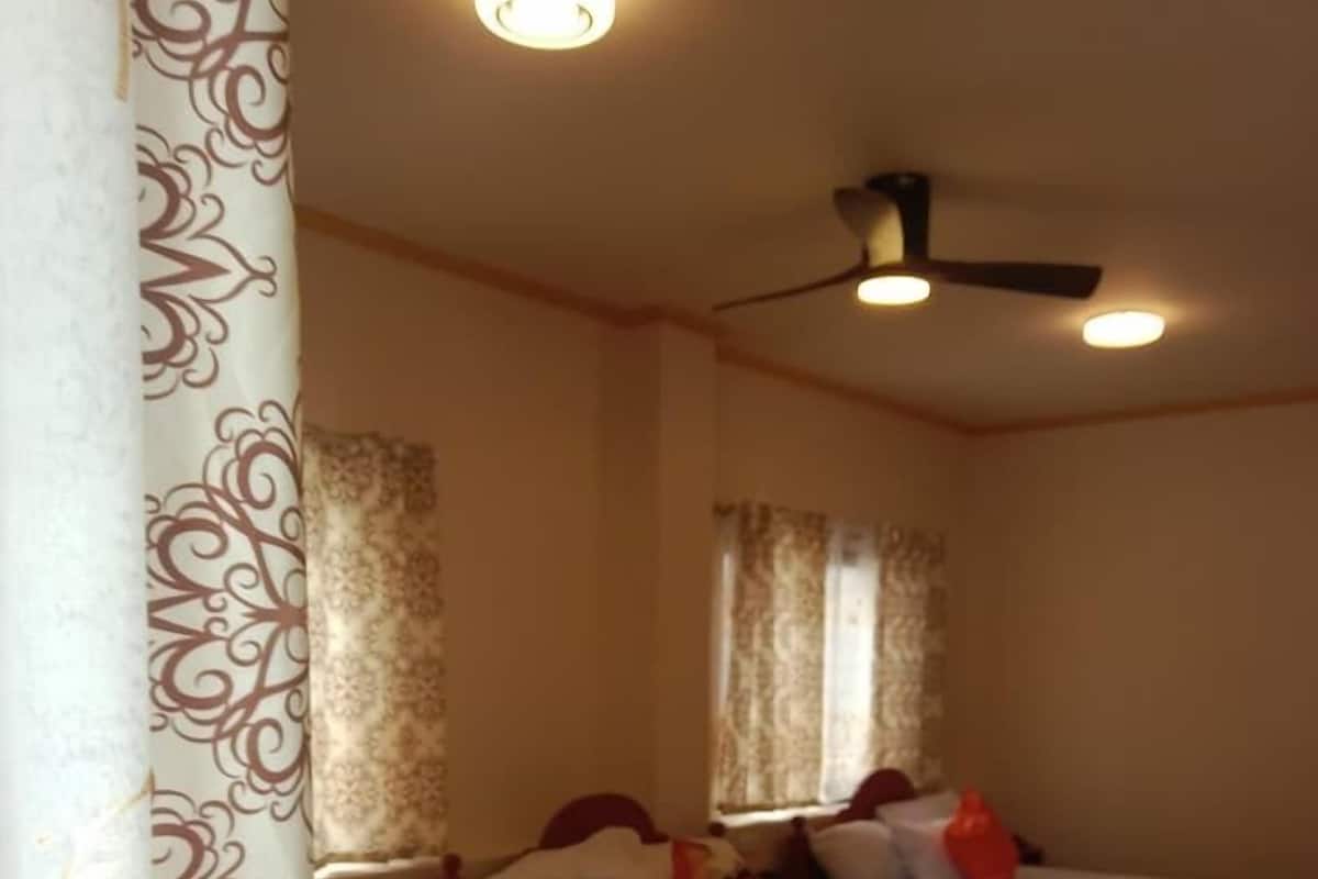 Une chambre d’hôtel avec trois lits simples, un ventilateur de plafond et une fenêtre avec des rideaux.