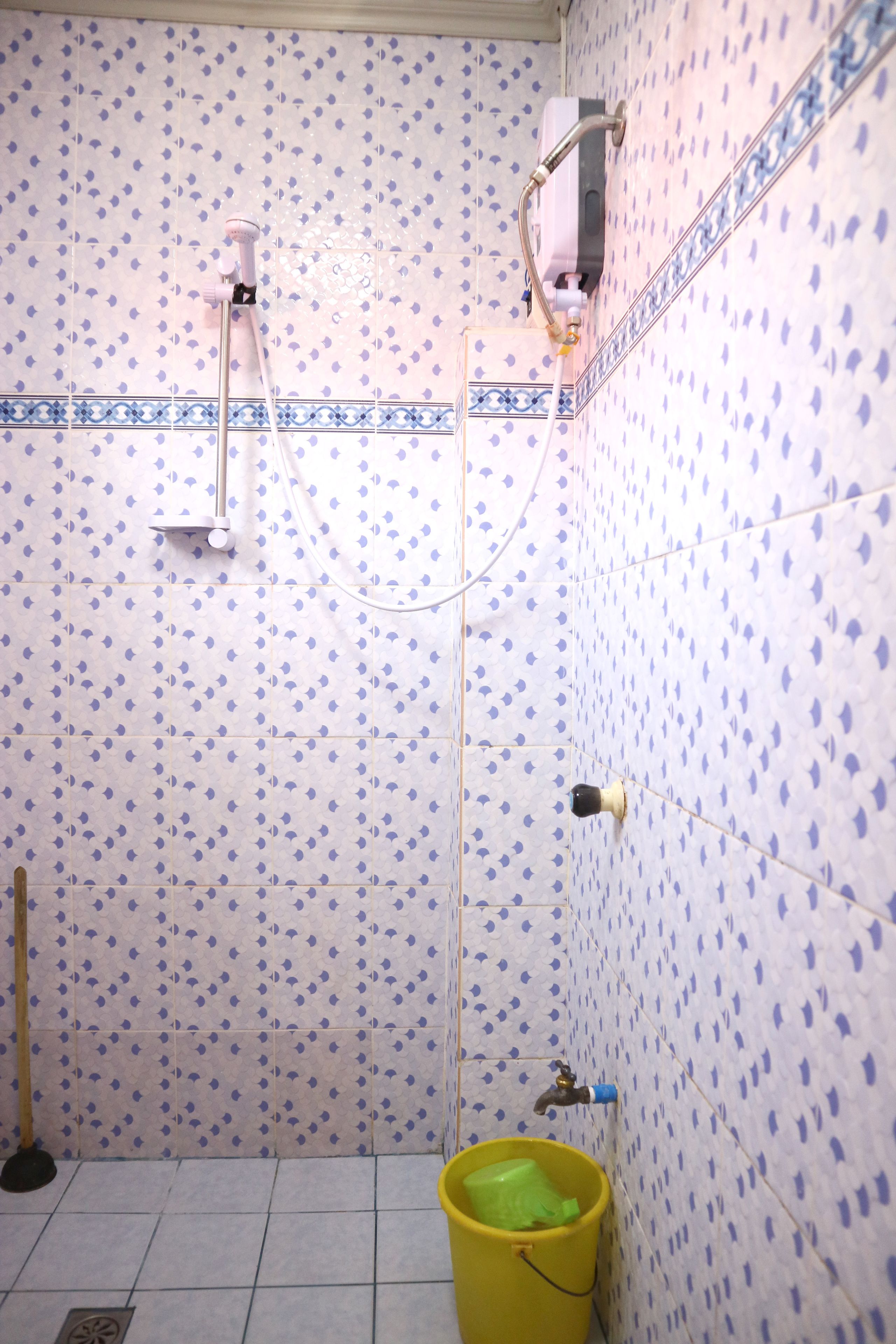 A bathroom with patterned tiles, a yellow bucket, and a showerhead.