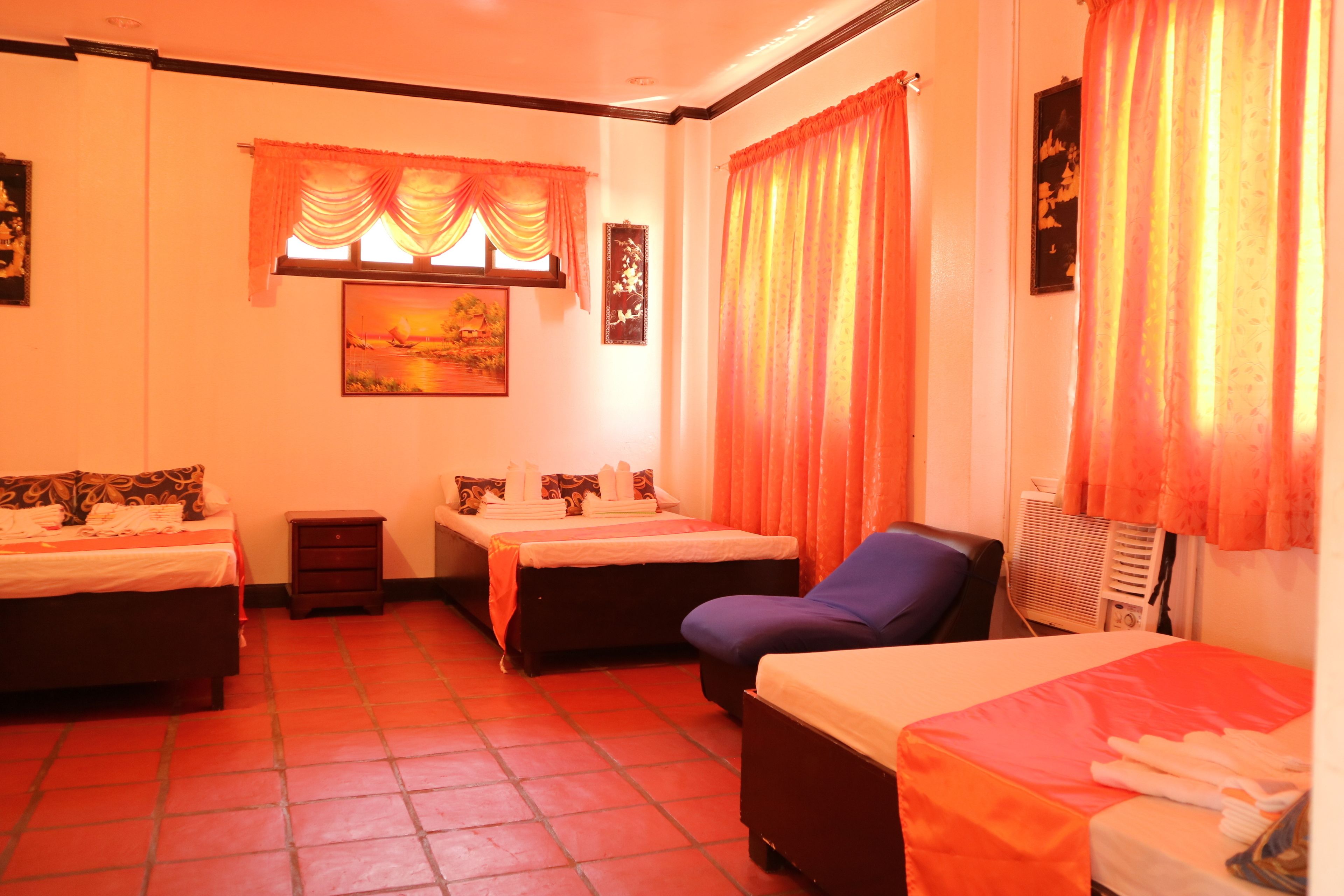 A hotel room with two beds, a chair, a small table, and a window with curtains.