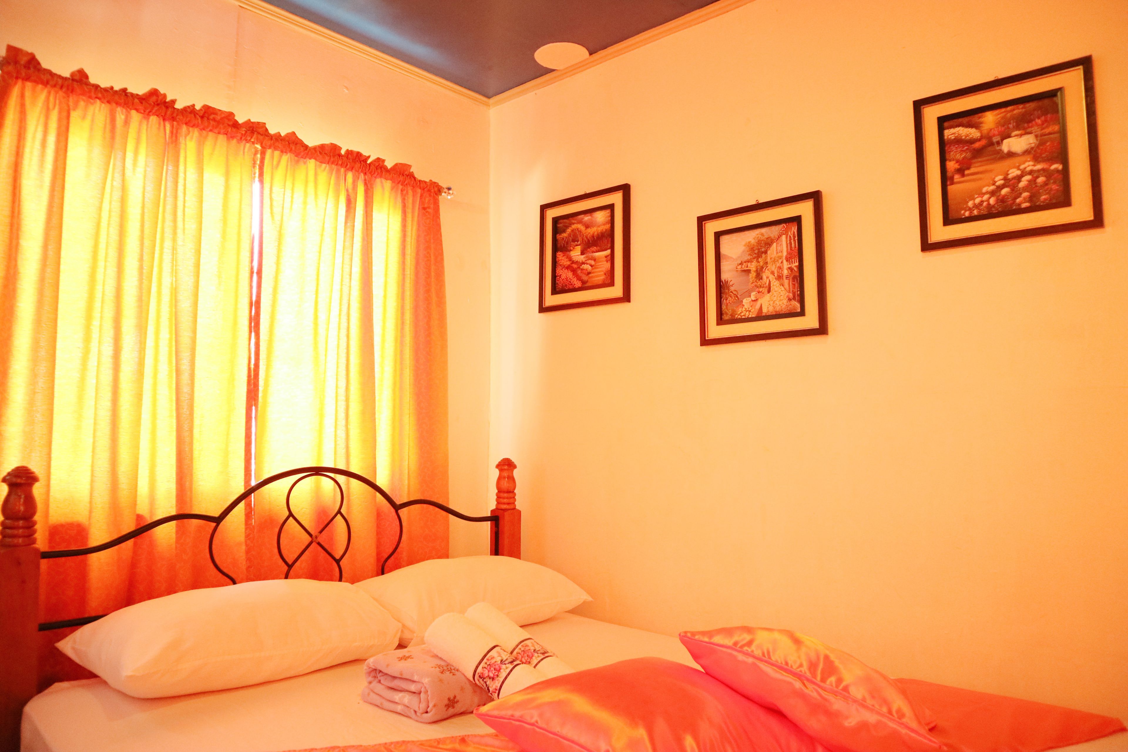 A bedroom with a bed, curtains, and three framed pictures on the wall.