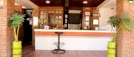 A brick building with a wooden ceiling, a counter with a stool, and potted plants.