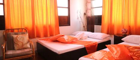 Habitación de hotel con dos camas, cortinas naranjas, una silla y un jarrón con ramas.