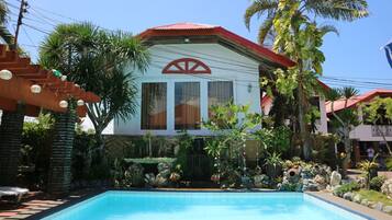 A house with a swimming pool, surrounded by tropical plants and palm trees.