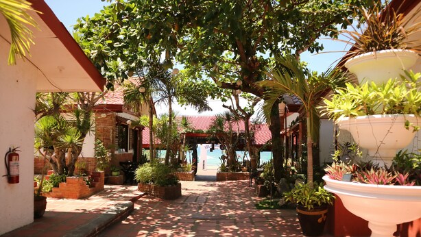 A courtyard with a tiled pathway, potted plants, and a building with a red roof. - Isla Bonita Beach Resort (San Juan)