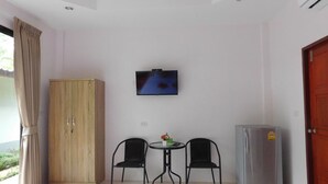 A room with a wooden wardrobe, a television mounted on the wall, a table with two chairs, and a refrigerator. - Phuket Sirinapha Resort (Sa Khu)